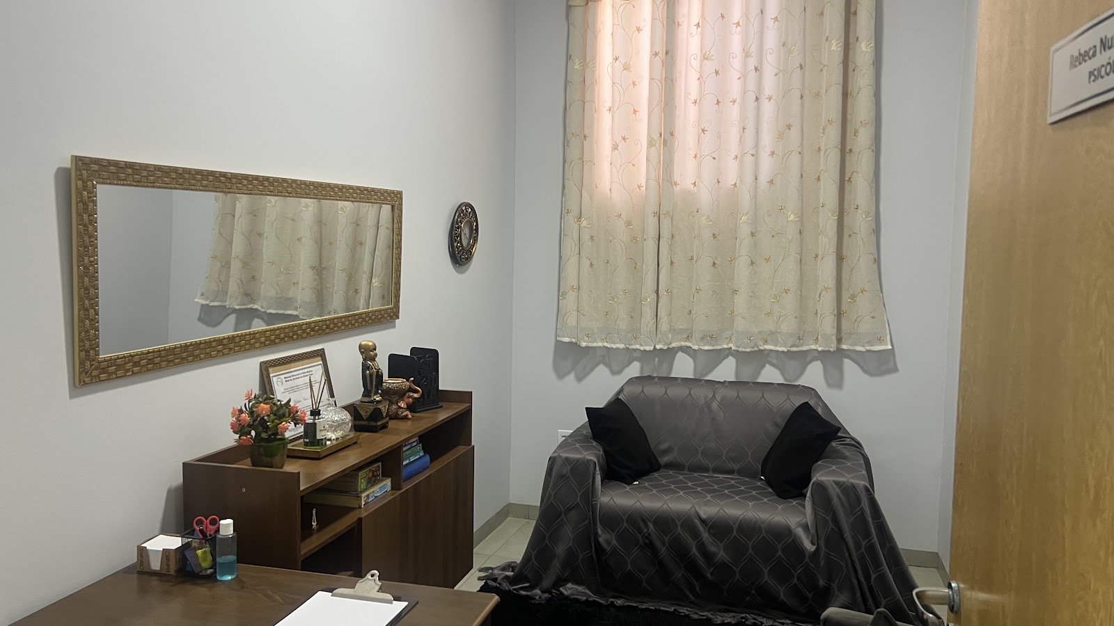 Consultório de atendimento da Rebeca Muniz na Clínica Bady, com mesa, espelho e sofá.